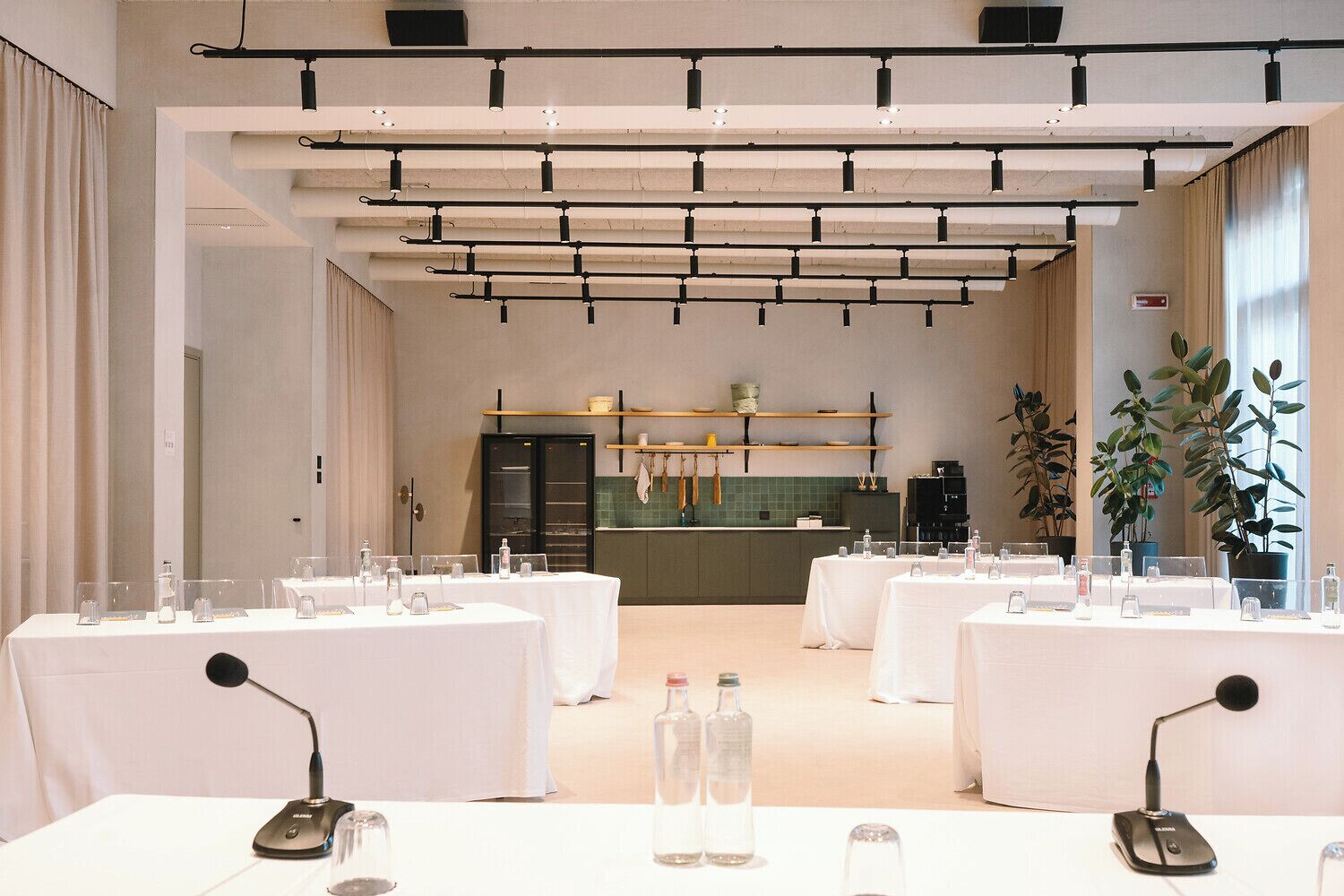 Un salón de conferencias con mesas dispuestas para una reunión, equipado con micrófonos y botellas de agua.