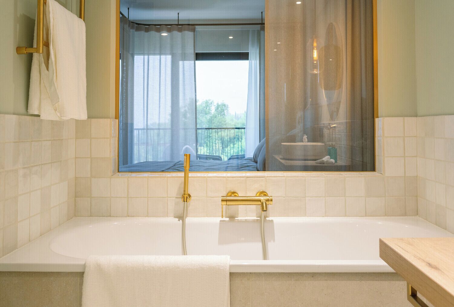 Un baño moderno con una bañera grande, una ventana con cortinas translúcidas y vistas a un balcón.