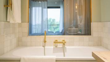 Un baño moderno con una bañera grande, una ventana con cortinas translúcidas y vistas a un balcón.