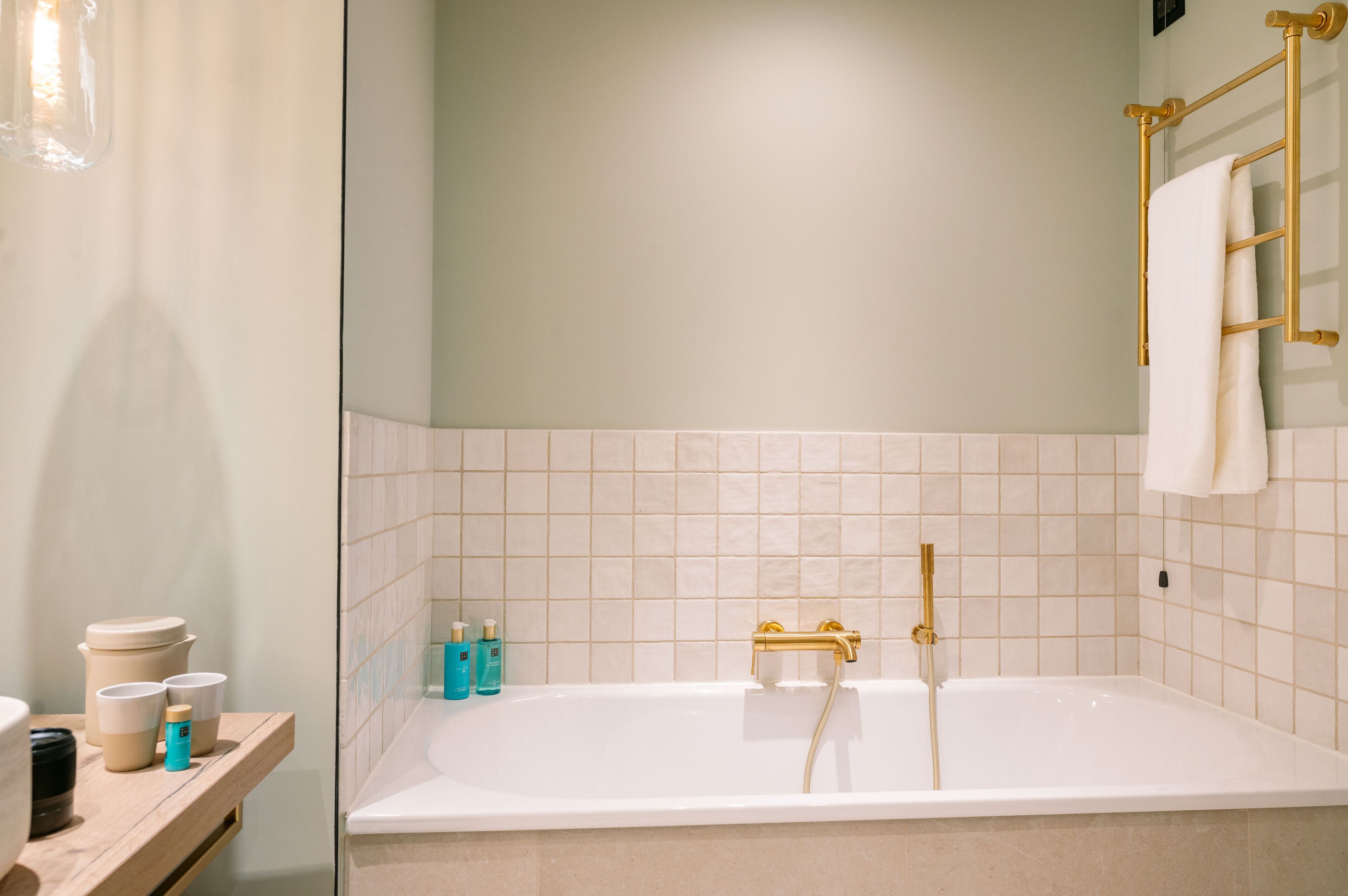 A modern bathroom with a white bathtub, gold fixtures, and a wooden vanity with toiletries.