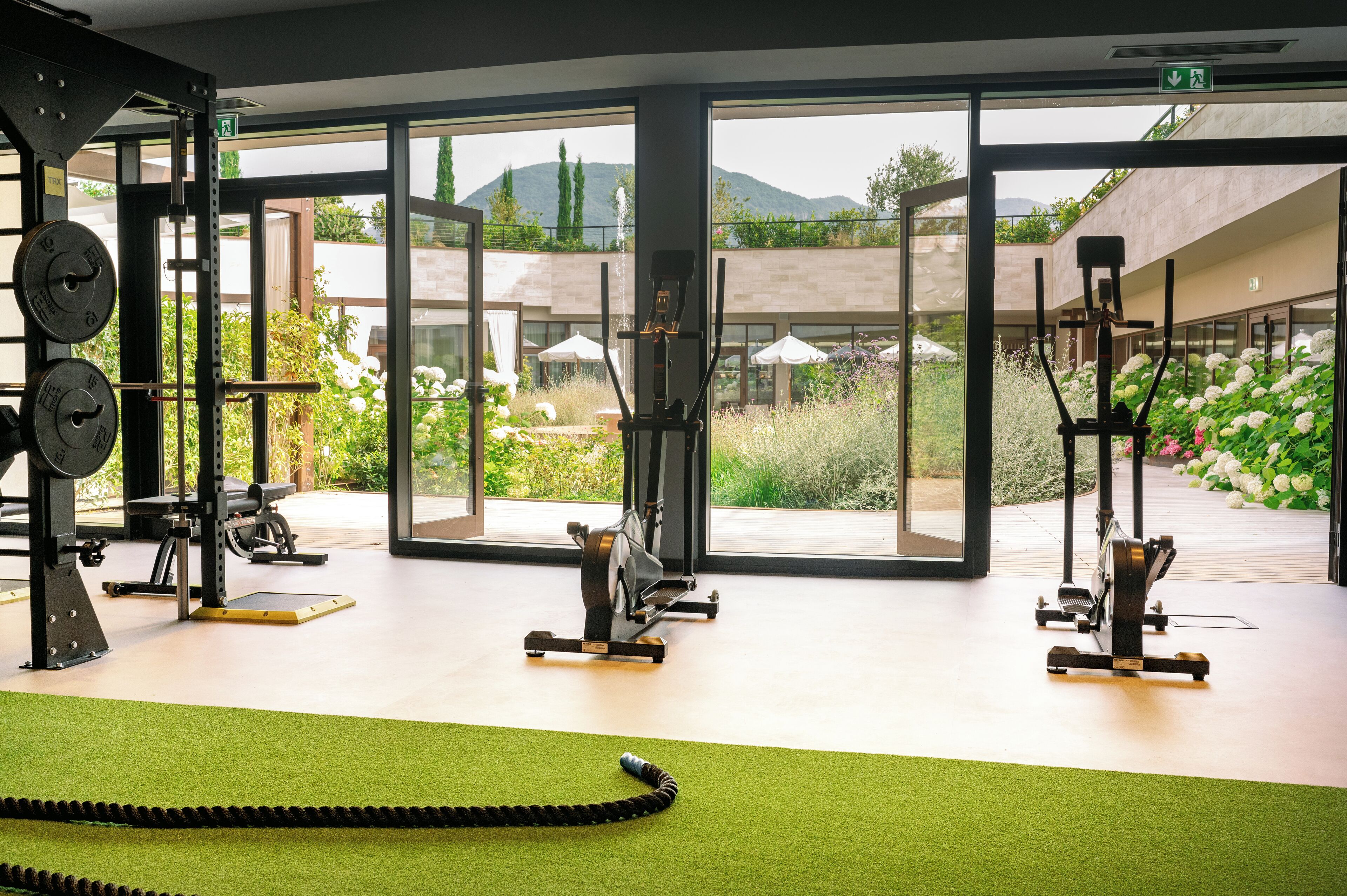 A gym with exercise equipment, large windows, and a view of greenery and mountains.