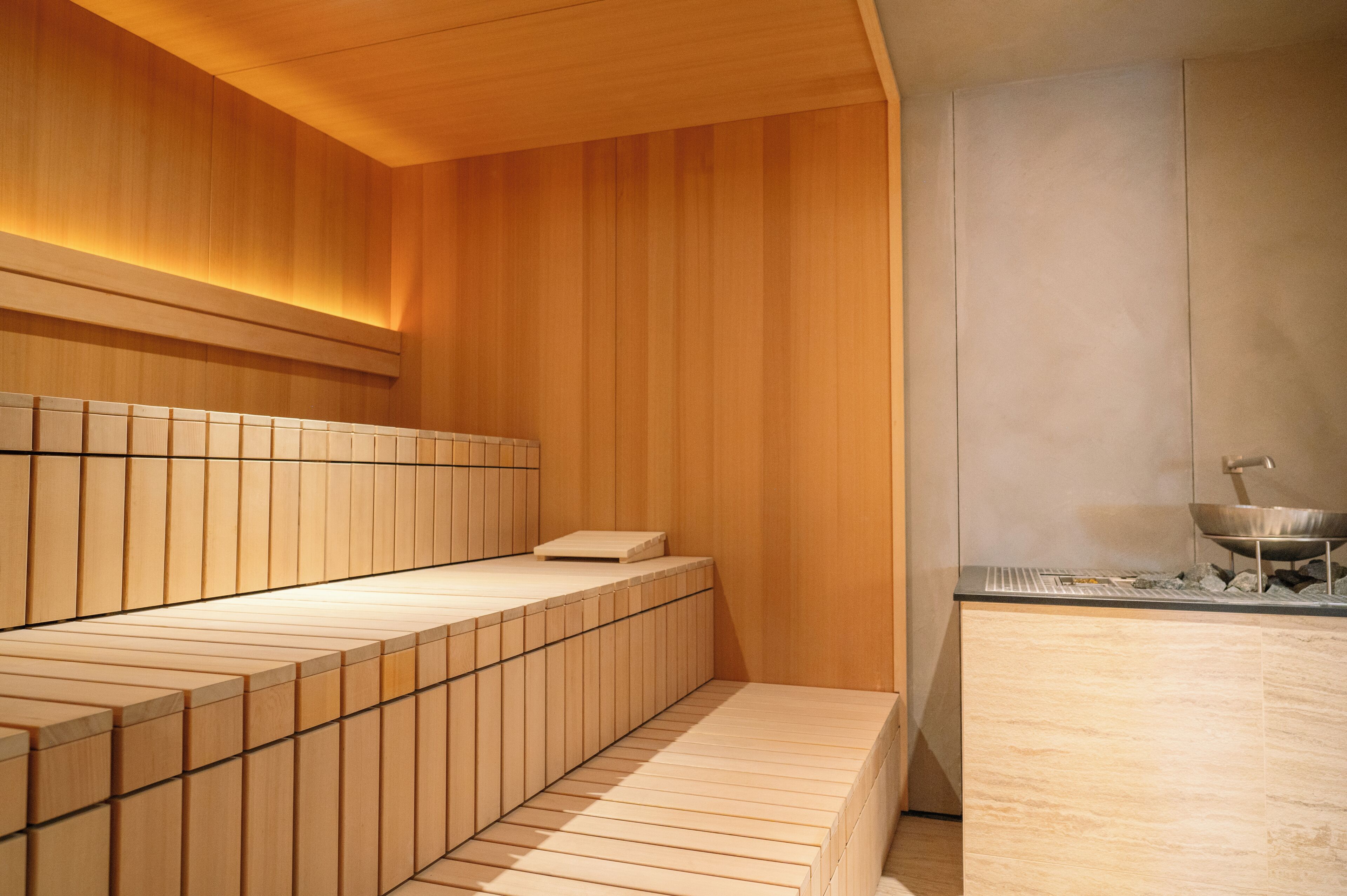 A modern sauna with wooden benches and a stone countertop with a wok.