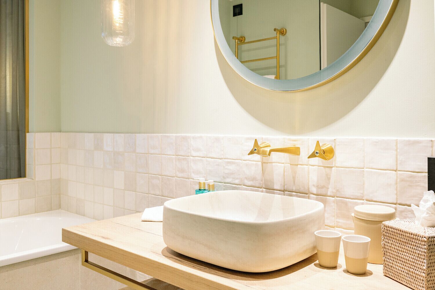 A bathroom with a large oval sink, a round mirror, and a bathtub.