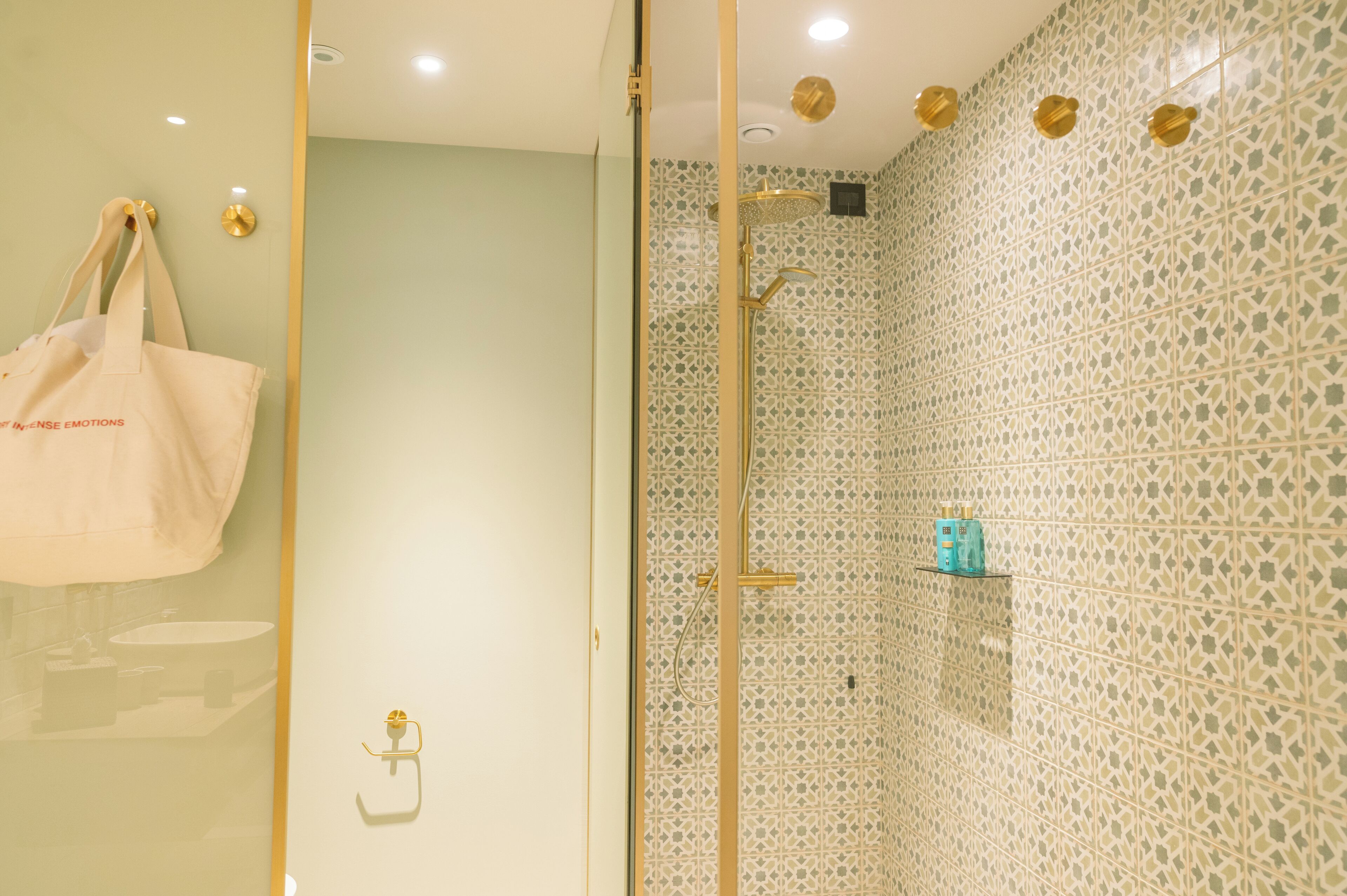 Un baño con pared de azulejos estampados, cabina de ducha de vidrio y una bolsa de tela color beige colgada en la pared.