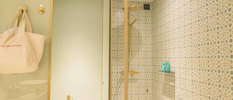 Un baño con pared de azulejos estampados, cabina de ducha de vidrio y una bolsa de tela color beige colgada en la pared.