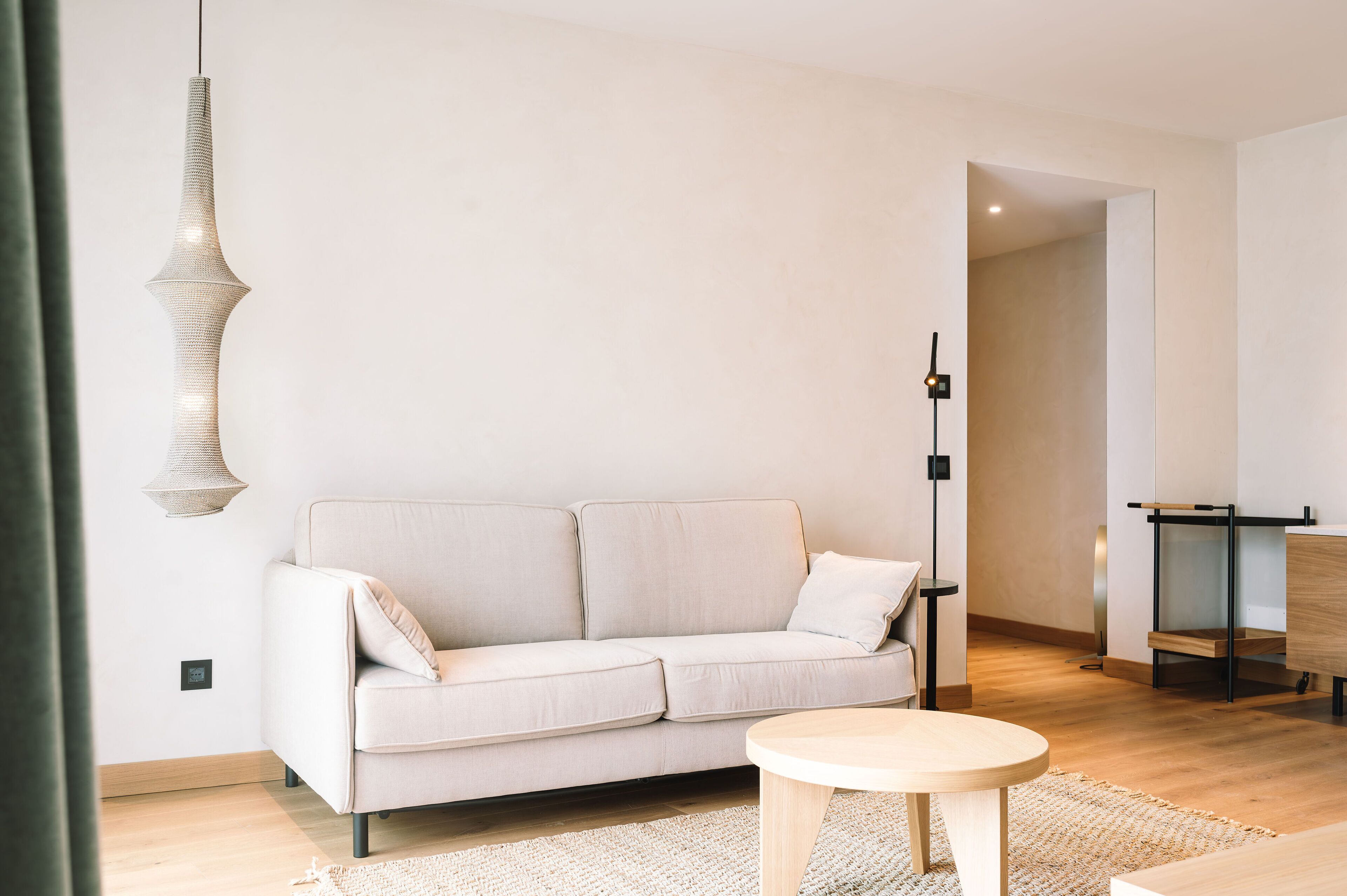 Un salon moderne avec un canapé de couleur claire, une table basse ronde en bois et un luminaire suspendu.
