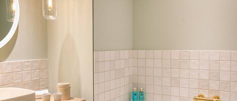 A bathroom with a round mirror, a wooden vanity, a white sink, a beige countertop, a white bathtub, and a shower with a gold faucet.