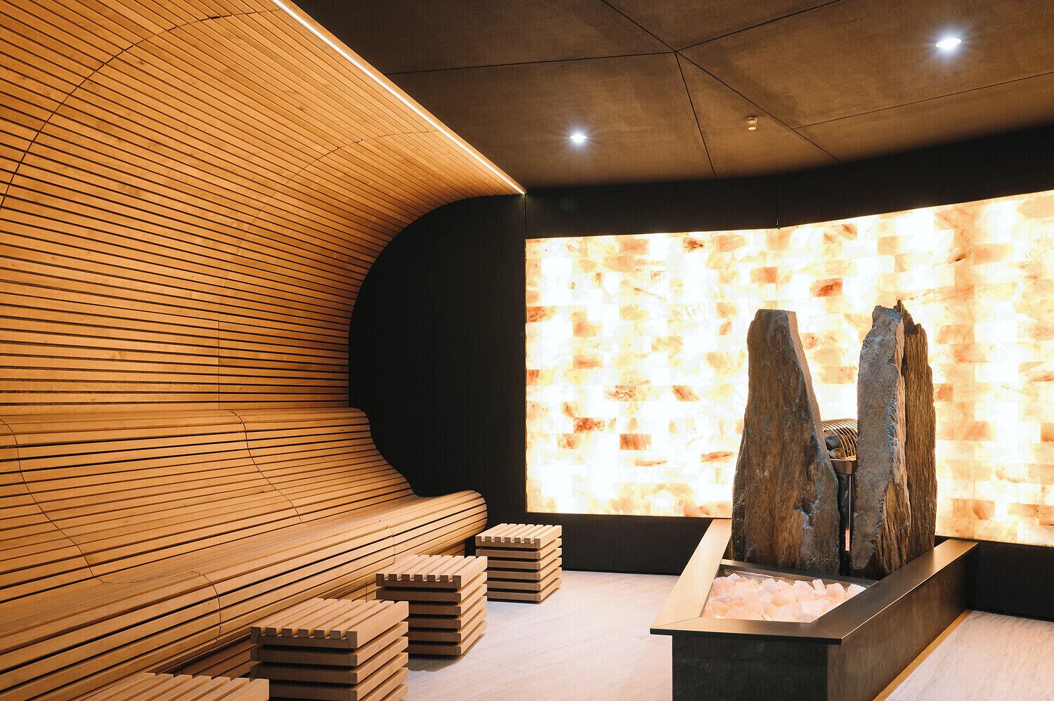 Un moderno espacio de spa con bancos de madera, pared de piedra y piscina de agua salada.