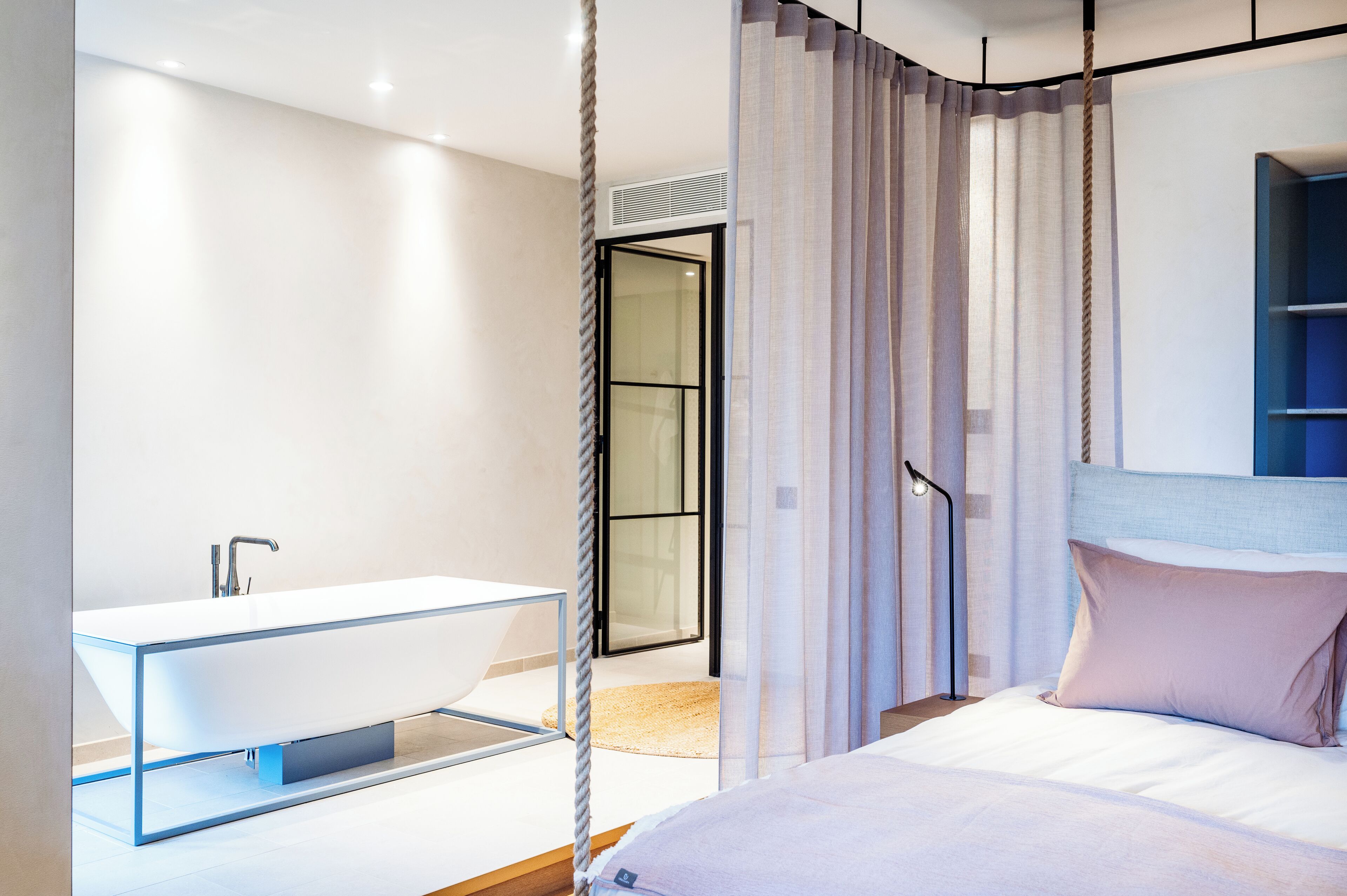 A modern bedroom with a large bed, a bedside table, a built-in shelf, and a bathroom with a modern sink and shower.