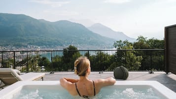 A person relaxing in a hot tub with a scenic view of mountains and a body of water.