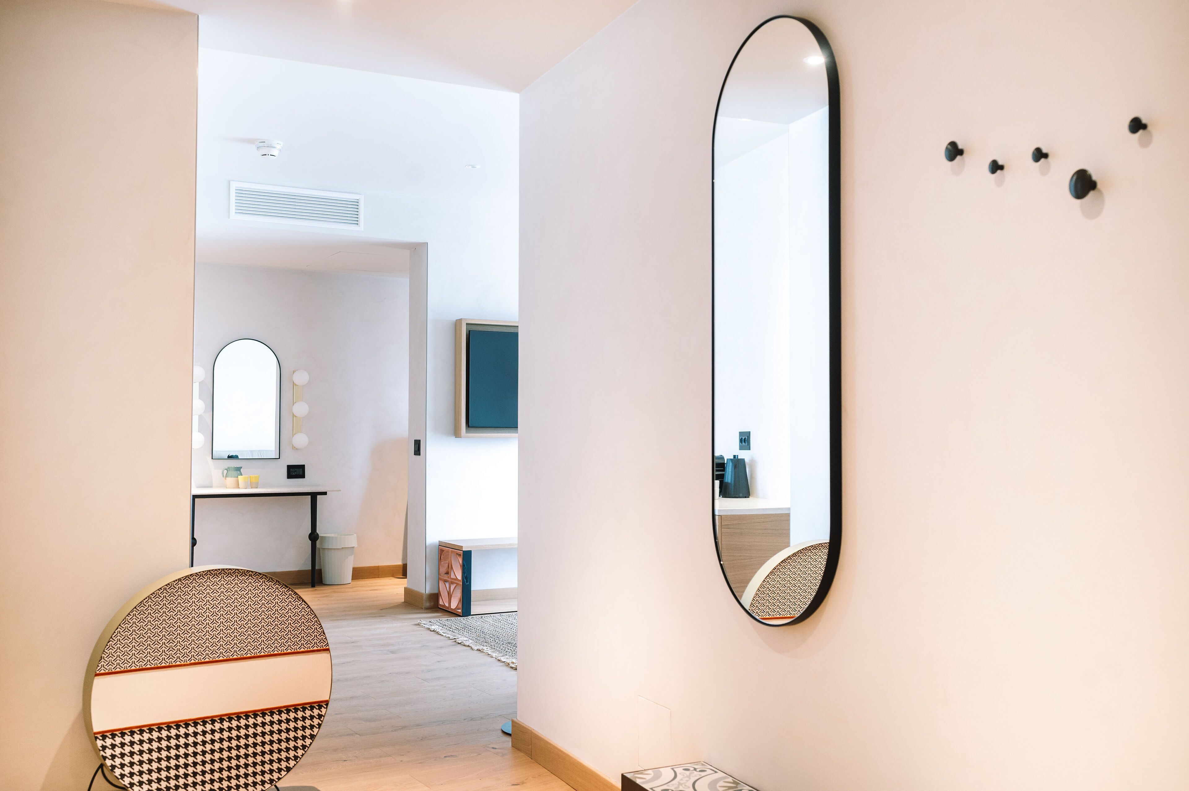 A modern interior with a round mirror, a vanity with a mirror, and a wall-mounted light fixture.