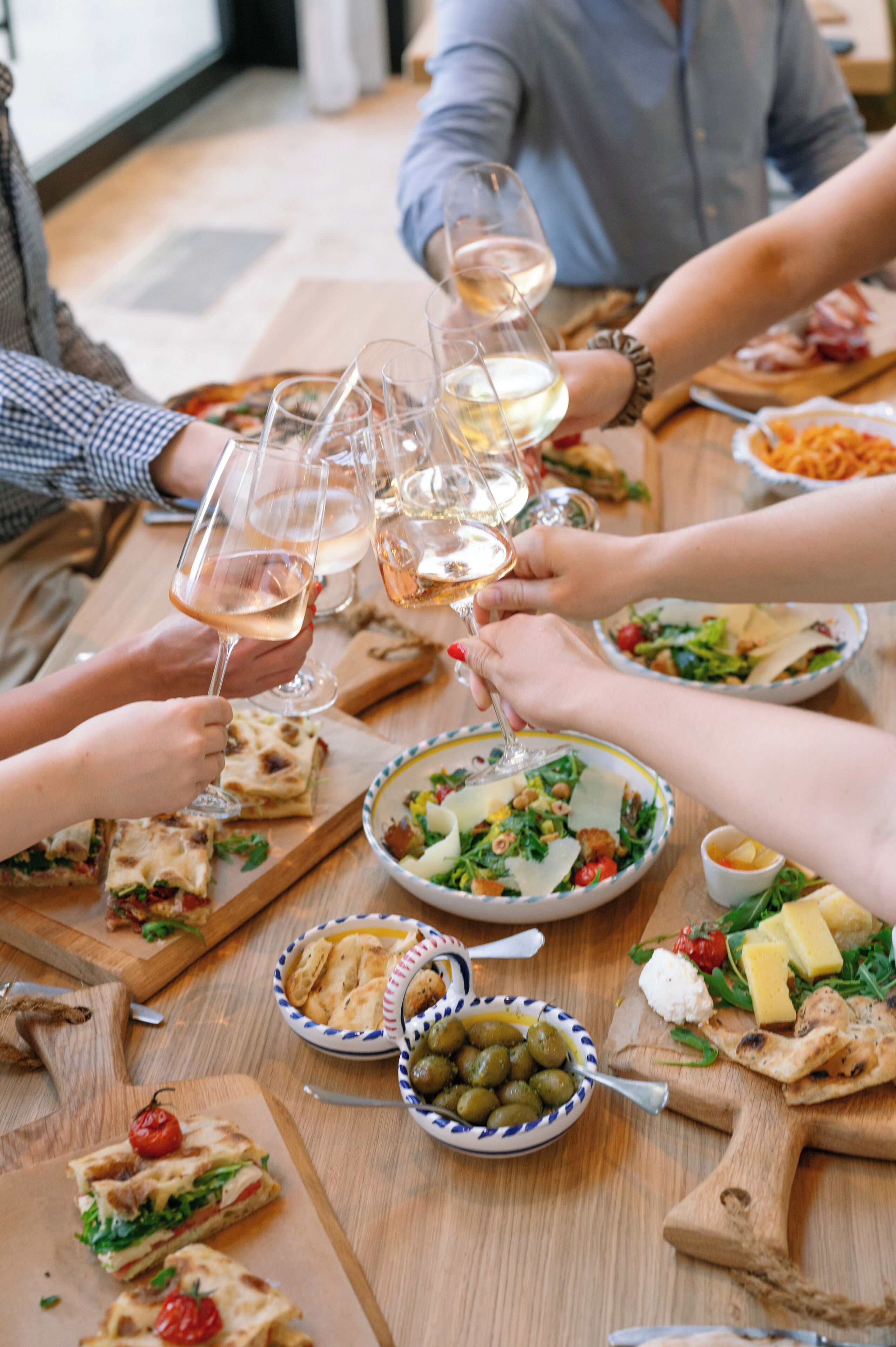 Un grupo de personas brindando con copas de vino alrededor de una mesa de madera con varios platos.