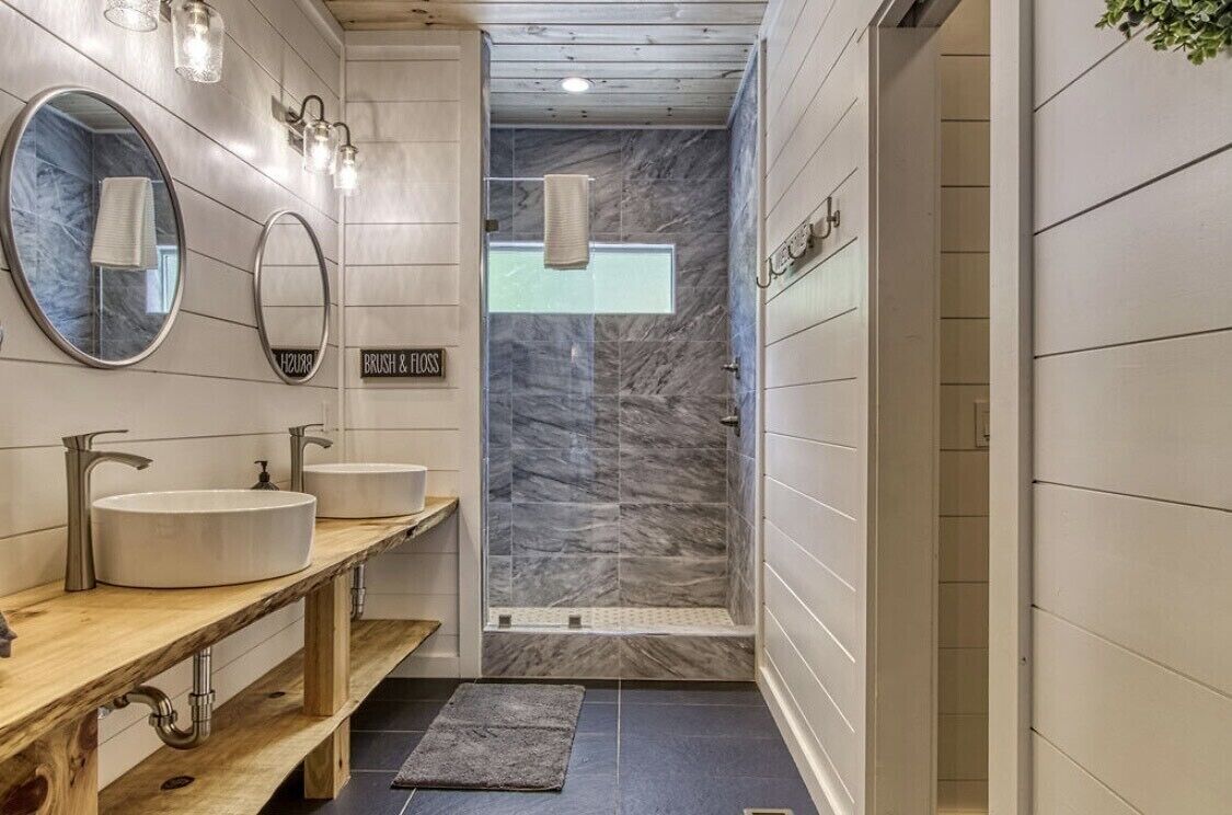 A modern bathroom with two sinks, a shower, and a wooden vanity.