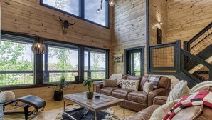 Ein geräumiges Wohnzimmer mit einer Ledersofa, einem Couchtisch und Blick ins Freie durch große Fenster.