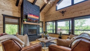 Ein gemütliches Wohnzimmer mit Ledersofas, einem Kamin und großen Fenstern mit Blick ins Freie.