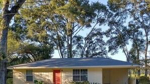 A single-story house with a red door, a front porch, and a driveway leading to the garage.