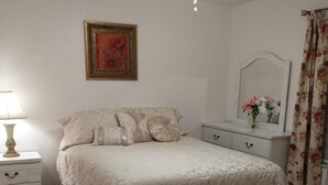 A bedroom with a bed, a nightstand, a dresser, a ceiling fan, a framed picture, and a mirror.