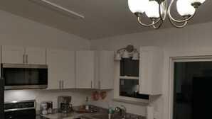 A modern kitchen with white cabinets, stainless steel appliances, a dining area with a table and chairs, and a chandelier.