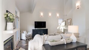Una sala de estar moderna con chimenea, televisor de pantalla plana, una mesa de centro de madera oscura y un sofá blanco.