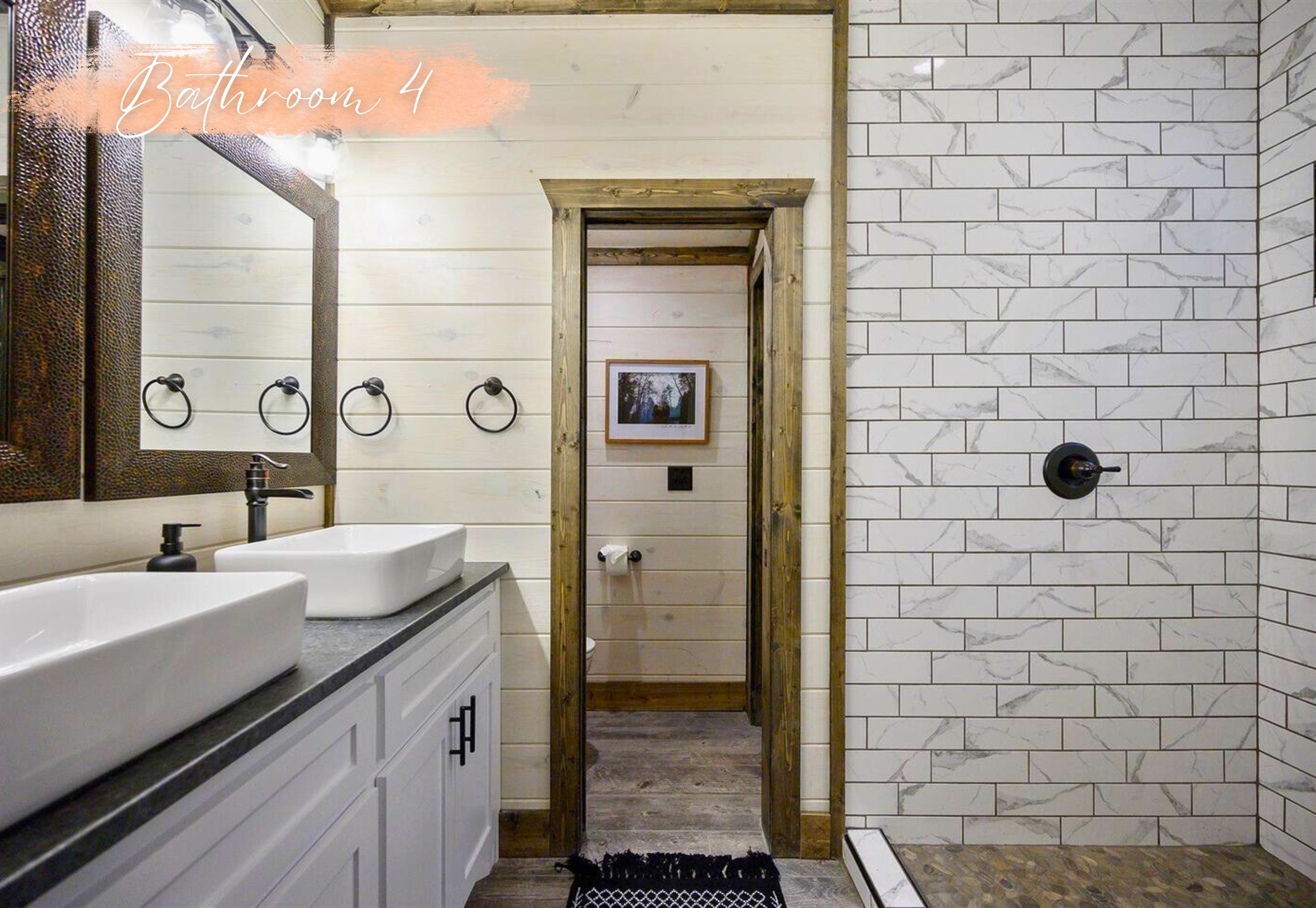 Une salle de bain avec deux lavabos, un miroir, une porte en bois et un espace douche aux carreaux de marbre blanc.