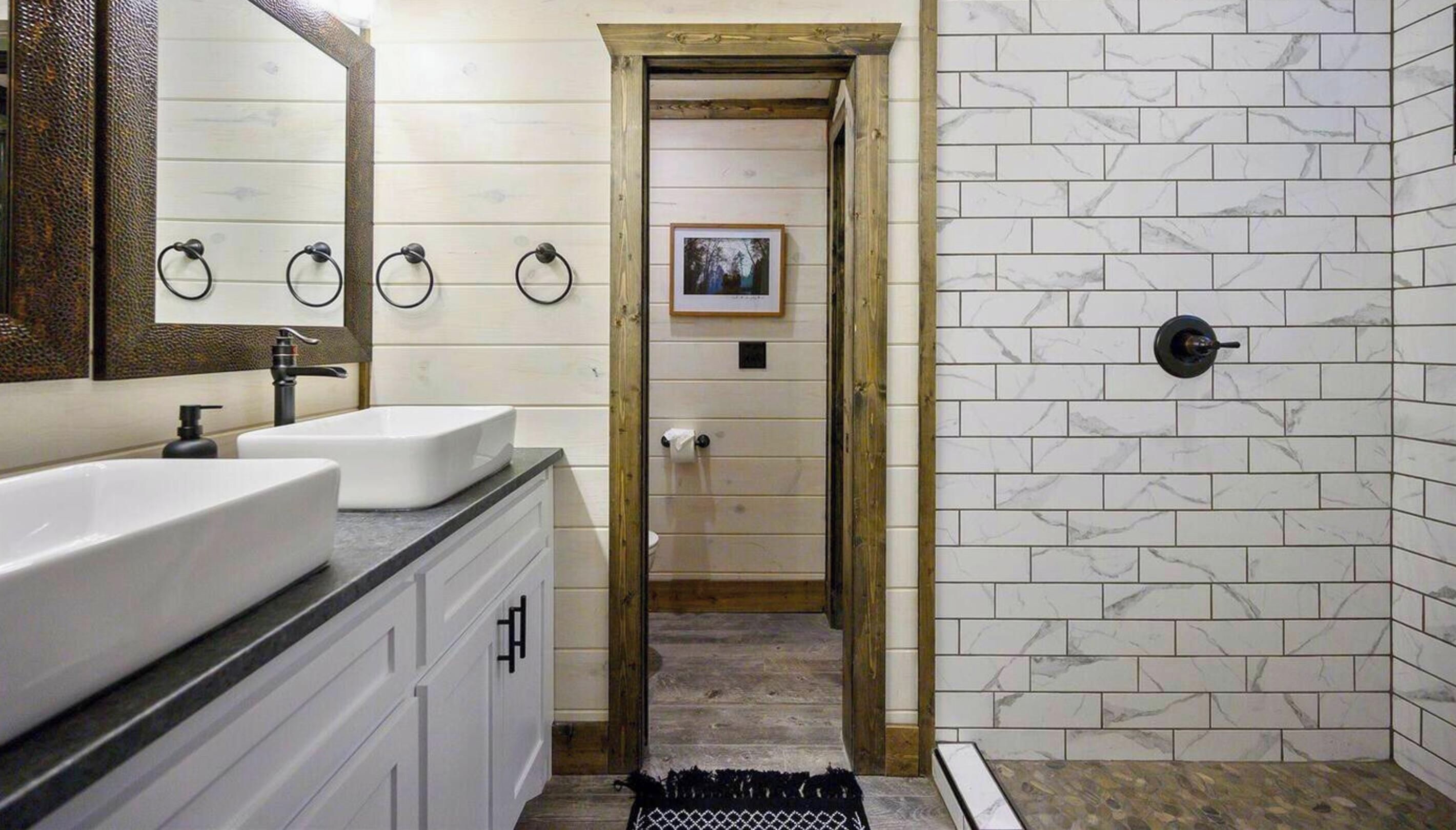 Een badkamer met een wit wastafelmeubel, een spiegel en een douchegedeelte met witte marmeren tegels.