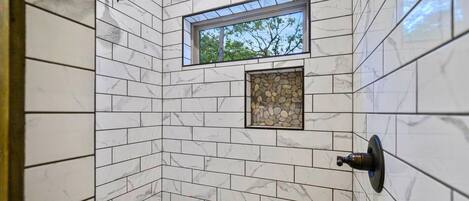 Une douche aux parois recouvertes de carreaux de marbre blanc, une fenêtre et un mur d’accent en pierre.