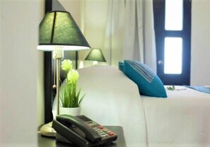 A hotel room with a bed, a bedside lamp, a telephone, and a potted plant.