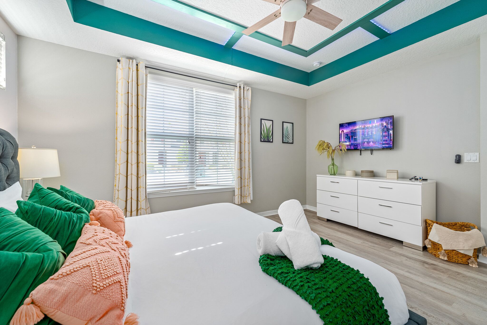 A modern hotel room with a large bed, a white dresser, a flat-screen TV, and a ceiling fan.
