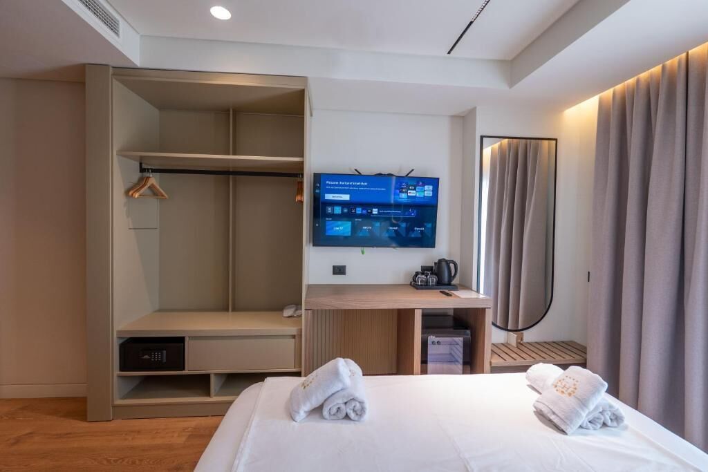 A hotel room with a bed, a desk with a computer, a TV, a wardrobe, and a mirror.