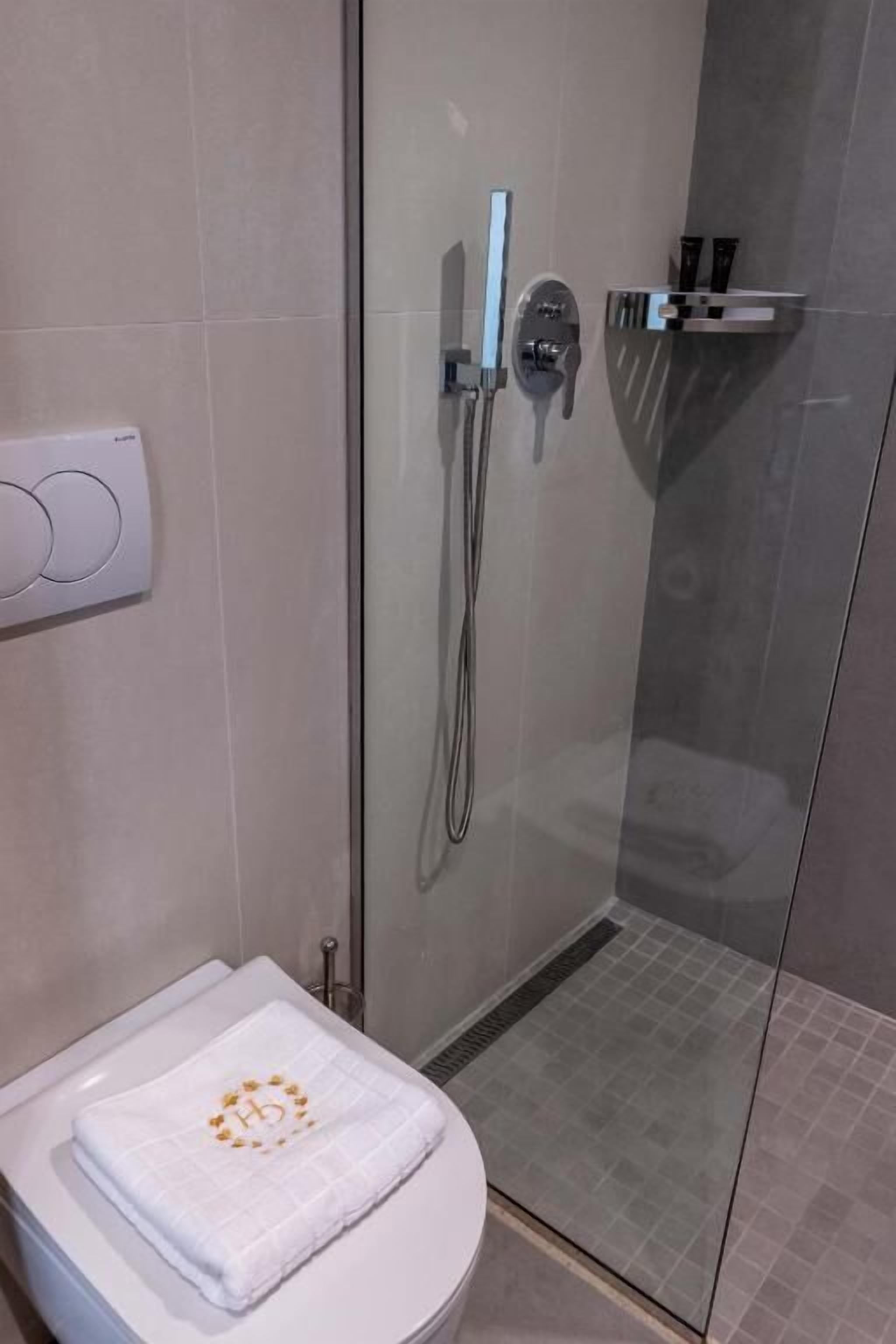 A modern bathroom with a glass-enclosed shower, a toilet with a white towel, and a wall-mounted control panel.