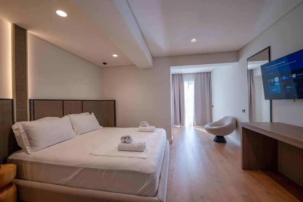 A modern hotel room with a large bed, a desk, and a television on the wall.