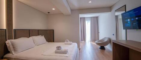 A modern hotel room with a large bed, a desk, and a television on the wall.