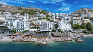 Un pueblo costero con edificios modernos, una playa con tumbonas y un cielo azul despejado.