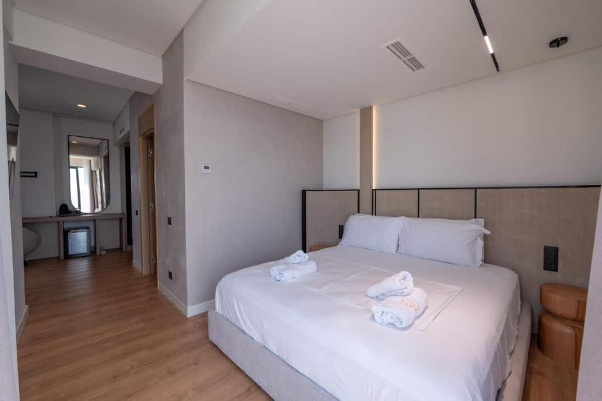 A modern hotel room with a large bed, a small desk, and a bathroom.
