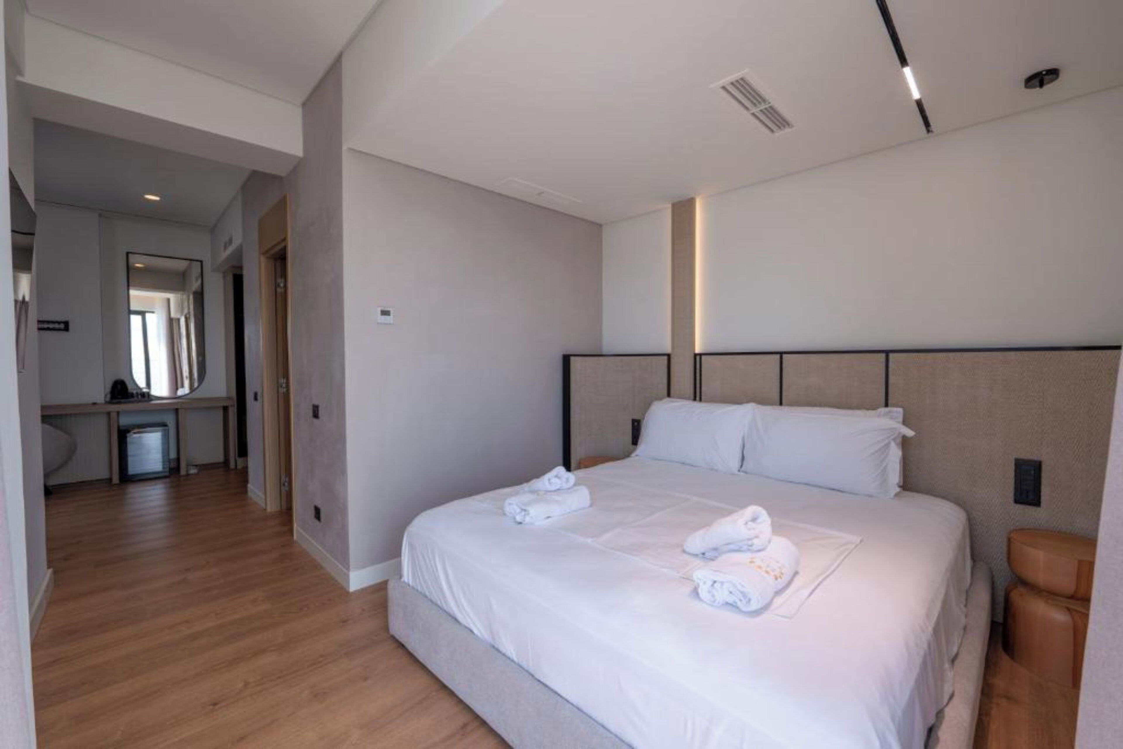 A hotel room with a large bed, a bedside table, a bathroom, and a hallway.