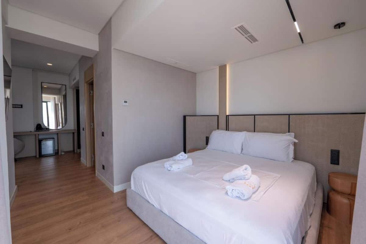 A hotel room with a large bed, a bedside table, a bathroom, and a hallway.