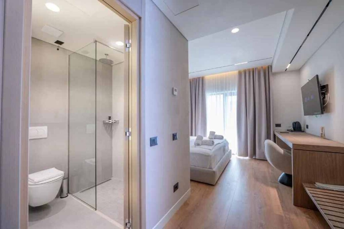 Una habitación de hotel moderna con ducha de vidrio, una cama, un escritorio y un televisor fijado a la pared.