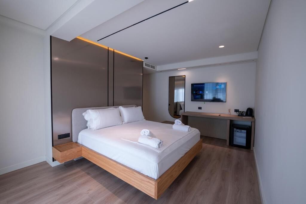 A modern hotel room with a wooden bed, a desk, and a flat-screen TV.
