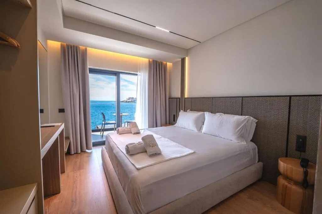A modern hotel room with a large bed, a desk, and a view of the sea.