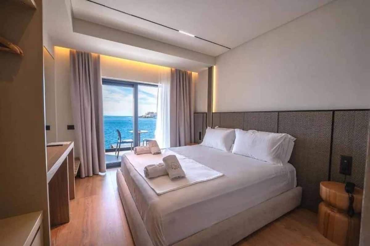 A modern hotel room with a large bed, a desk, and a view of the sea.
