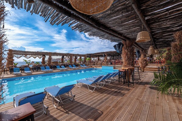 A poolside area with lounge chairs, tables, and a wooden deck. - Grand Hotel Saranda (Sarandë)