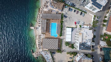 Vista aèria d'un hotel a la costa, amb piscina, seients al costat de la platja i una zona d'aparcament.