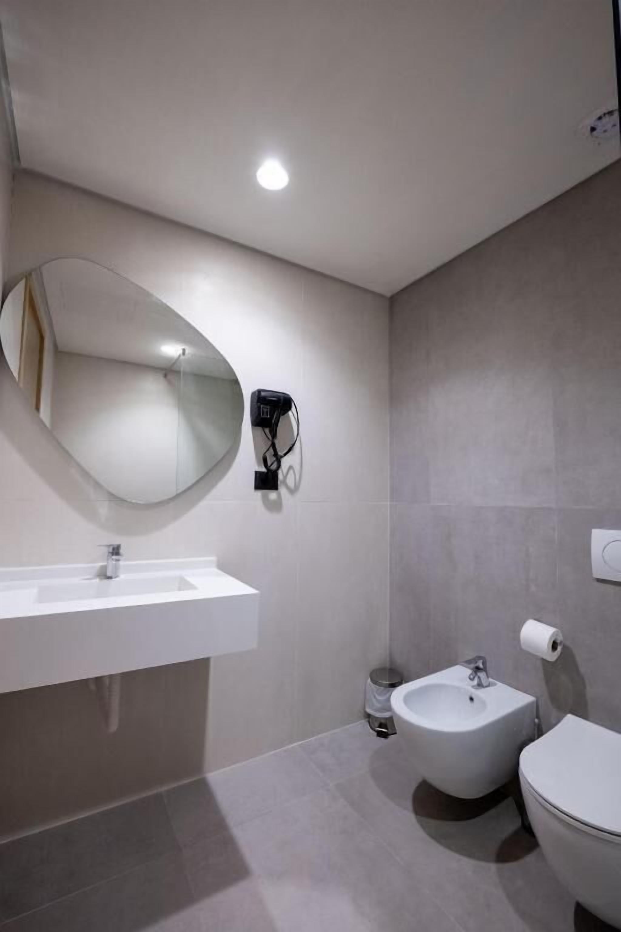 A modern bathroom with a large mirror, a sink, a bidet, and a toilet.