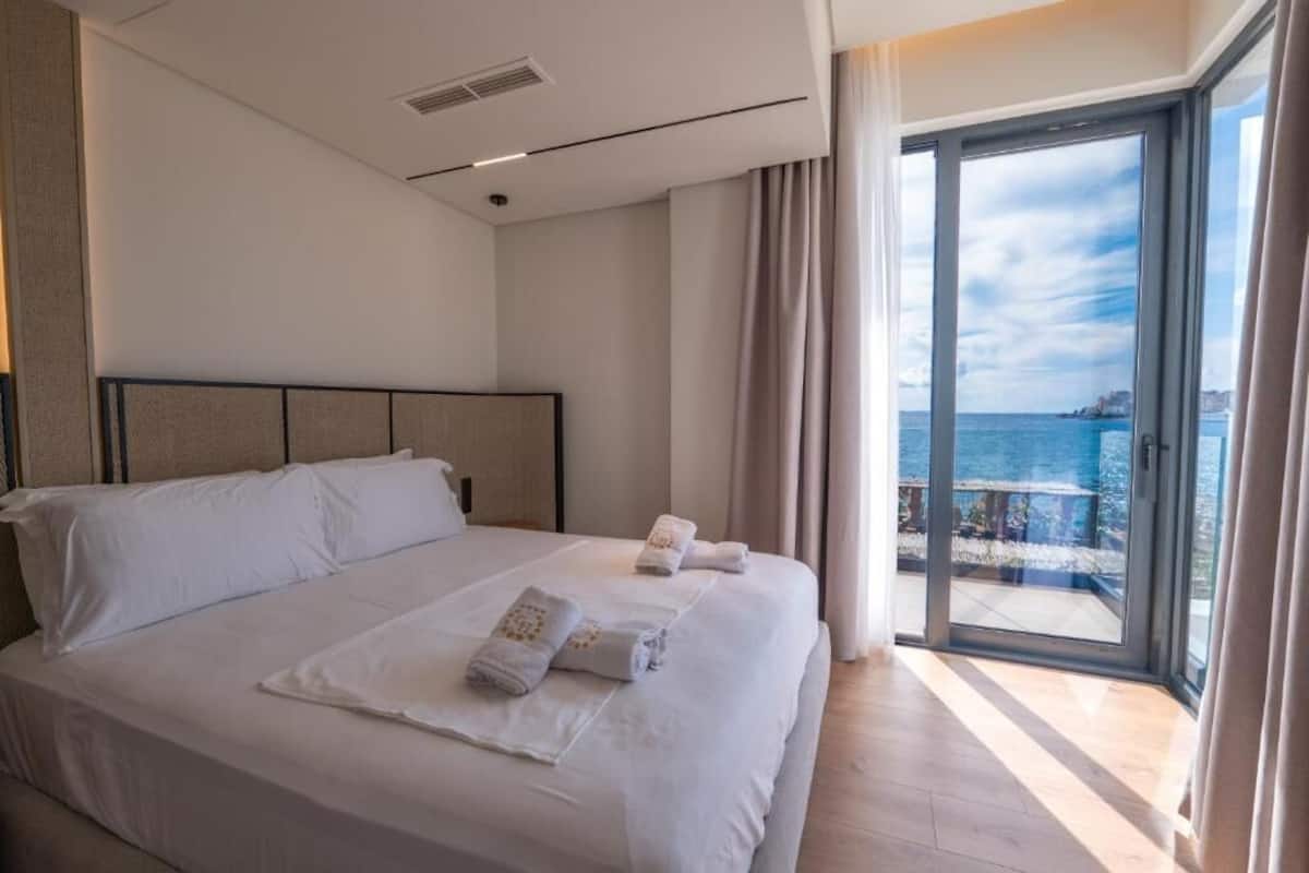 A modern hotel room with a large bed, a view of the sea, and a balcony.