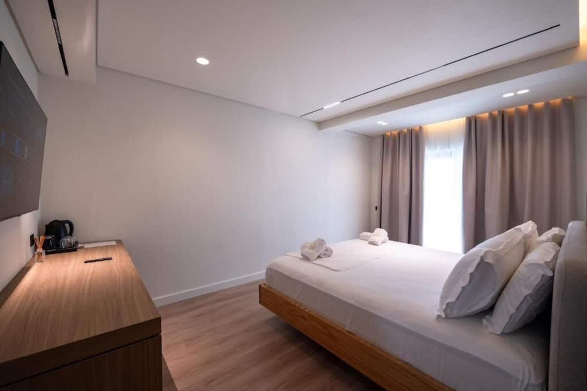 A modern bedroom with a bed, bedside table, and a TV mounted on the wall.