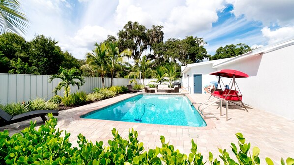 A rectangular swimming pool with a tiled deck, surrounded by lush greenery and a white fence. - 2 Acre 4BR Coastal Hideout: Heated Salt Pool Games (Bradenton)
