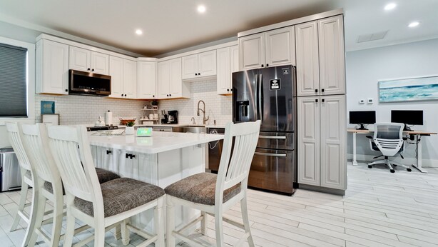A modern kitchen with white cabinetry, a stainless steel refrigerator, and a dining area with white chairs.