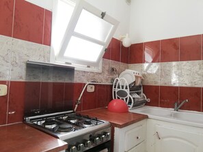 A kitchen with a gas stove, a sink, a dish rack, and a window.