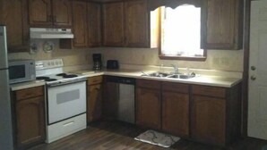 Cocina compacta con muebles de madera, estufa, microondas y lavavajillas.