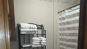 Un baño con inodoro, lavamanos, toallero con toallas dobladas y cortina de ducha.